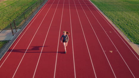 Teen-girl-athlete-on-a-running-track-warms-up-towards-and-under-aerial-camera
