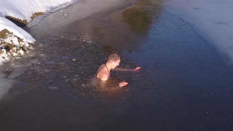 Young-man-under-water-in-partially-frozen-mountain-lake-rises-to-the-surface-and-turns-to-exit