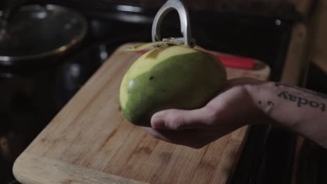 Canada---Peeling-Of-Green-Unripe-Mango-With-A-Peeler-Over-The-Wooden-Chopping-Board---Closeup-Shot