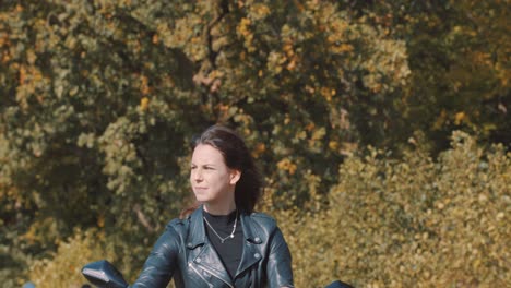 Front-view-of-beautiful-woman-hair-waving-in-wind,-Female-Biker-wearing-leather-jacket-On-road-with-autumn-leaf-color-Trees-at-amelisweerd-forest-on-sunny-day