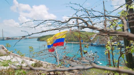 Kolumbianische-Flagge-Weht-Im-Wind-Eines-Schoners,-Der-In-Einem-Tropischen-Paradies-Angedockt-Ist