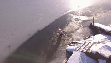 Man-standing-in-frozen-mountain-like-wearing-shorts-no-shirt-breaks-ice-with-hand-to-clear-hole-for-ice-swimming-and-polar-plunge