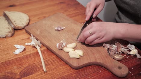 Woman's-hands-with-a-knife-crush-the-garlic-on-a-chopping-board,-then-peel-the-skin-2