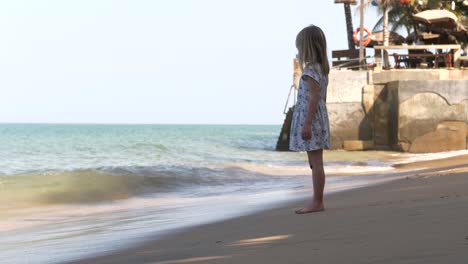 Young-dreamy-vacation-girl-in-summer-dress-on-tropical-beach-looking-out-at-sea,-Long-shot