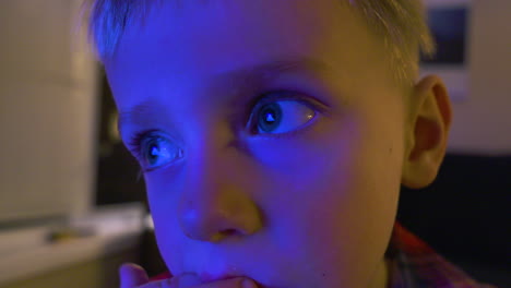 Close-up-of-a-little-boy's-illuminated-face-as-he-watches-TV-and-eats-a-snack