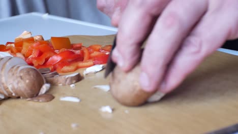 Close-up-shallow-focus-on-chopped-red-peppers-ingredient-as-male-hands,-blurred-in-foreground-chop---slide-nutritious-mushrooms