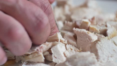Close-up-on-male-hands-with-finger-tattoo,-chopping---preparing-fresh-cooked-chicken-pieces-for-nutritious,-healthy-meal