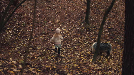 Little-girl-runs-down-hill-covered-in-autumn-leaves-with-dog-nearby