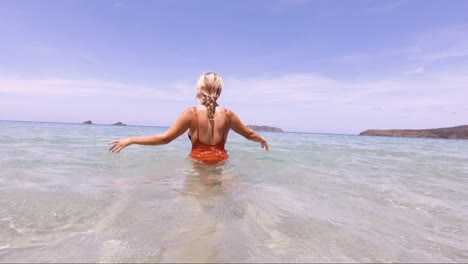 Slow-motion-shot-from-underwater-to-above-water-showing-a-Young-Beautiful-Woman-sits-in-the-crystal-clear-oceans-of-Nacpan-Beach-in-El-Nido-Philippines,-perfect-holiday-and-dream-destination