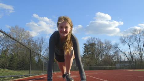 Teen-girl-in-the-ready-position-on-a-track-smiles-as-she-looks-down-the-track