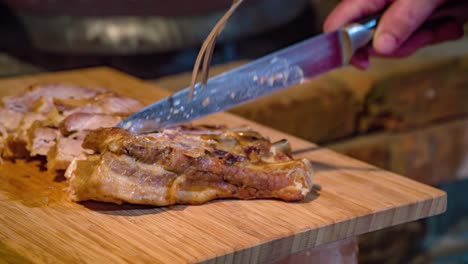 Close-up-shot-of-a-chef-cutting-tender-slices-of-pork-meat-near-a-wooden-fired-oven