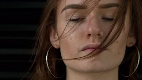 Slow-motion-close-up-shot-of-a-pretty-young-woman-with-brown-hair-partially-covering-her-face,-facing-the-camera-with-a-serious-expression