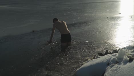 Man-standing-in-frozen-lake-breaking-ice-with-hands-so-he-can-swim