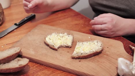 Woman's-hands-take-a-cut-slice-of-bread-smeared-with-butter-and-garlic-on-a-cutting-board