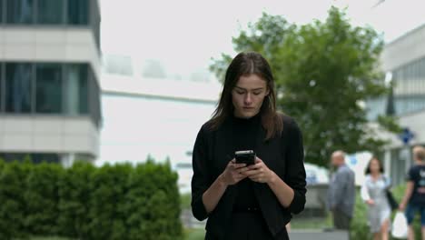 A-young-woman-with-brown-hair-walks-towards-the-camera,-looking-intensely-at-her-mobile-phone