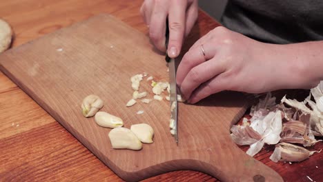 Woman's-hands-with-a-knife-chops-two-cloves-of-garlic-on-a-chopping-board