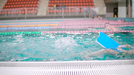 Junge-Schwimmt-Und-Paddelt-Mit-Den-Beinen-In-Einem-Großen-Olympischen-Pool