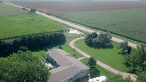 Drone-aerial-view-of-a-sprawling-home,-farm-yard,-standing-water,-corn-fields-and-a-gravel-road-in-rural-Nebraska,-USA