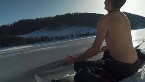 Hombre-Sin-Camisa-Respirando-Fuertemente-Hiperventilando-Mientras-Se-Sienta-Al-Lado-Del-Lago-Congelado