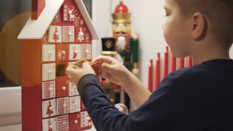 Happy-Little-Boy-Takes-Sweet-From-Advent-Calendar-House-Form-With-Christmas-Nutcrackers-in-Background-1