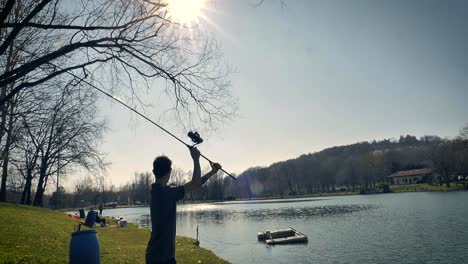 Morning-sun-shines-on-a-lake-as-a-young-man-casts-his-line-with-a-long-fishing-pole-and-spinning-reel