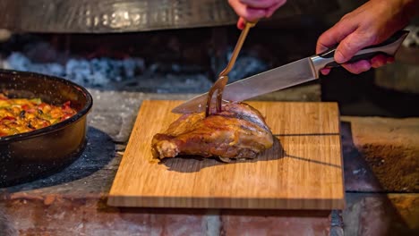 Close-up-shot-of-a-person-cutting-a-piece-of-roasted-meat-on-a-wood-board