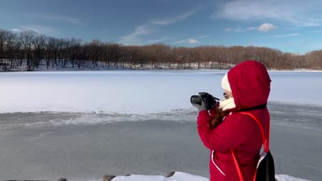 Girl-using-a-DSLR-camera-taking-photos-of-a-landscape-near-a-frozen-lake-in-winter