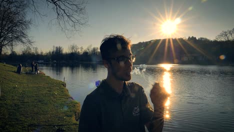 Man-inhales-deeply-from-a-cigarette-while-standing-beside-a-lake-at-sunset