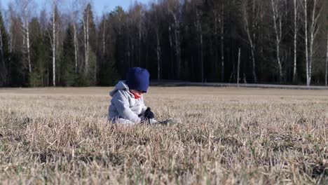 Toddler-boy-sitting-alone-in-rural-fiel,-springtime