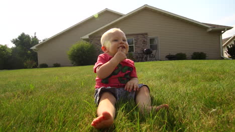 A-baby-sits-in-the-grass-sucking-his-finger-and-smiling