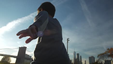 Young-boy-running-from-Manhattan-Bridge-toward-sunset-and-Brooklyn-Bridge-on-grassy-field