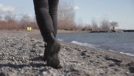 Back-View-Of-A-Woman-Feet-Walking-Along-The-Lake-Shore-During-Sunny-Day---Close-Up-Shot