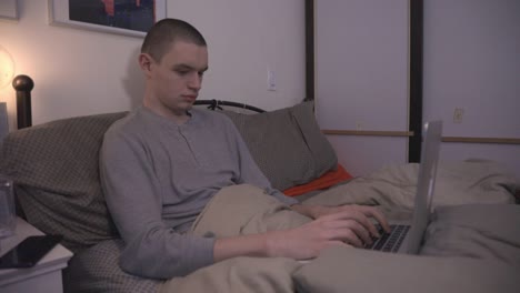 Junger-Mann,-Der-Nachts-Auf-Seinem-Bett-Arbeitet-Und-Einen-Laptop-Benutzt