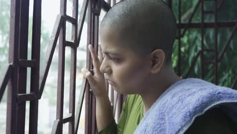 Sick-and-bald-Cancer-patient-young-Indian-girl-looking-outside-through-window-and-upset