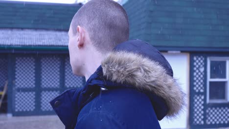 A-Man-Wearing-Winter-Coat-Standing-Outside-His-House-While-Looking-Around-With-Falling-Snow-In-Canada---Close-Up-Shot