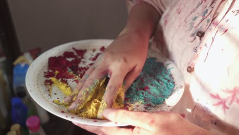 Unrecognizable-girl's-hand-plays-with-colored-powder-on-plate-at-home-on-Holi,-Indian-festival-of-colors,-lockdown-due-to-covid-19-corona-virus-quarantine,-slow-motion