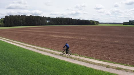 Aerial-wide-shot-of-a-man-riding-a-bike-on-a-small-dirt-road