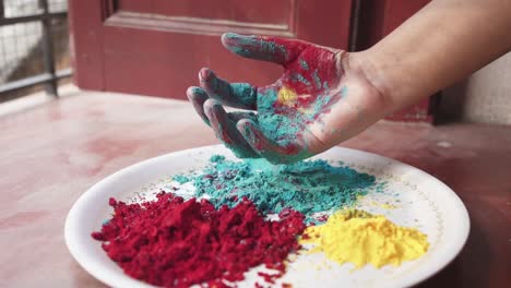 Hand-playing-with-coloured-powders-from-plate-on-Holi,-Indian-festival-at-home-due-to-covid-19-lockdown,-slow-motion