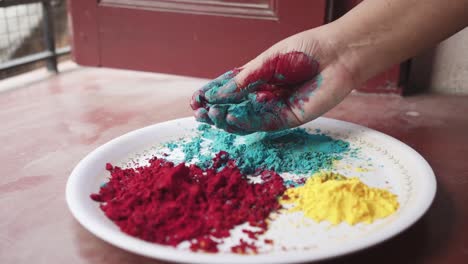 Hand-playing-with-color-powders-on-plate-on-Holi,-Indian-festival-at-home-due-to-pandemic-covid-19-coronavirus-lockdown,-Cinematic-closeup,-slow-motion