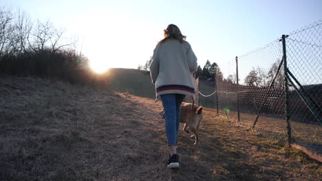 Young-Woman-Holding-A-Leash-Of-Her-Dog-And-Walking-On-The-Uphill-Trail-With-Bright-Sunrise-On-The-background-In-Ružomberok,-Liptov,-Slovakia