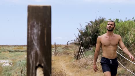 Young-Caucasian-strong-healthy-Lebanese-man-hiking-on-dirt-trail-wearing-shorts-and-shirtless,-Tripoli,-Lebanon,-close-up-slow-motion