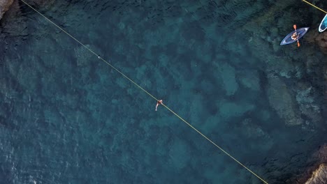 Zenital-Zoom-In-Drone-view-of-a-man-slackline-over-the-crystal-clear-waters-of-Ibiza