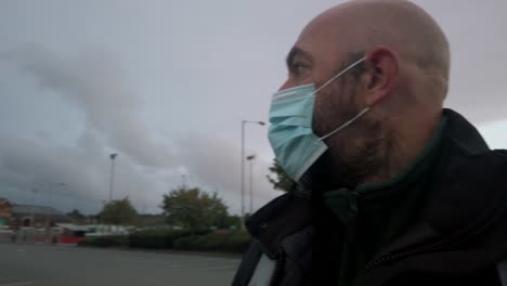 Male-in-workplace-wearing-uniform-and-PPE-face-mask-against-corona-virus-walking-car-park