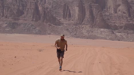 Adventurer-running-through-arid-desert,-mountains-at-the-background,-Wadi-Rum,-Jordan,-static-shot