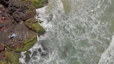 4k-Aerial-Top-Down-Drone-Shot-of-a-beautiful-27-year-old-young-Indian-woman-in-White-and-Blue-dress-relaxing-on-top-of-a-Cliff-being-crushed-by-the-sea-waves