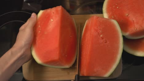 Hand-Firmly-Holding-A-Half-Sliced-Watermelon-Side-Down-Slicing-In-Half-Lengthwise-With-A-Sharp-Knife---Closeup-Shot