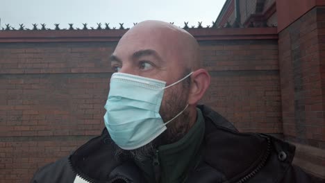 Male-security-guard-fixes-protective-corona-virus-medical-PPE-mask-in-front-of-high-brick-wall