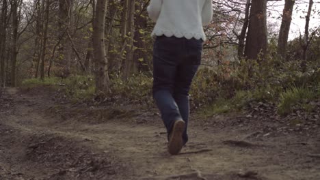 Woman-walks-on-countryside-path-through-woodland-wide-panning-shot