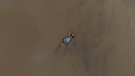 4k-Aerial-Top-down-Vortex-Drone-shot-of-a-pretty-27-year-old-Indian-girl-laying-on-the-sand-in-tranquility-along-the-sea-shore-of-Varkala