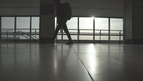 Traveler-walking-through-airport-hall,-sun-flare,-static-shot,-low-angle